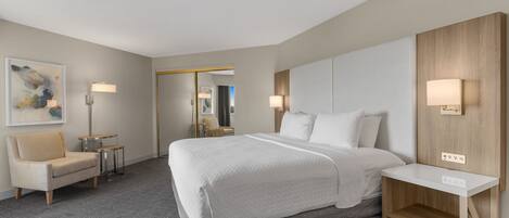 A modern hotel room with a large bed, a desk, a chair, and a small table.