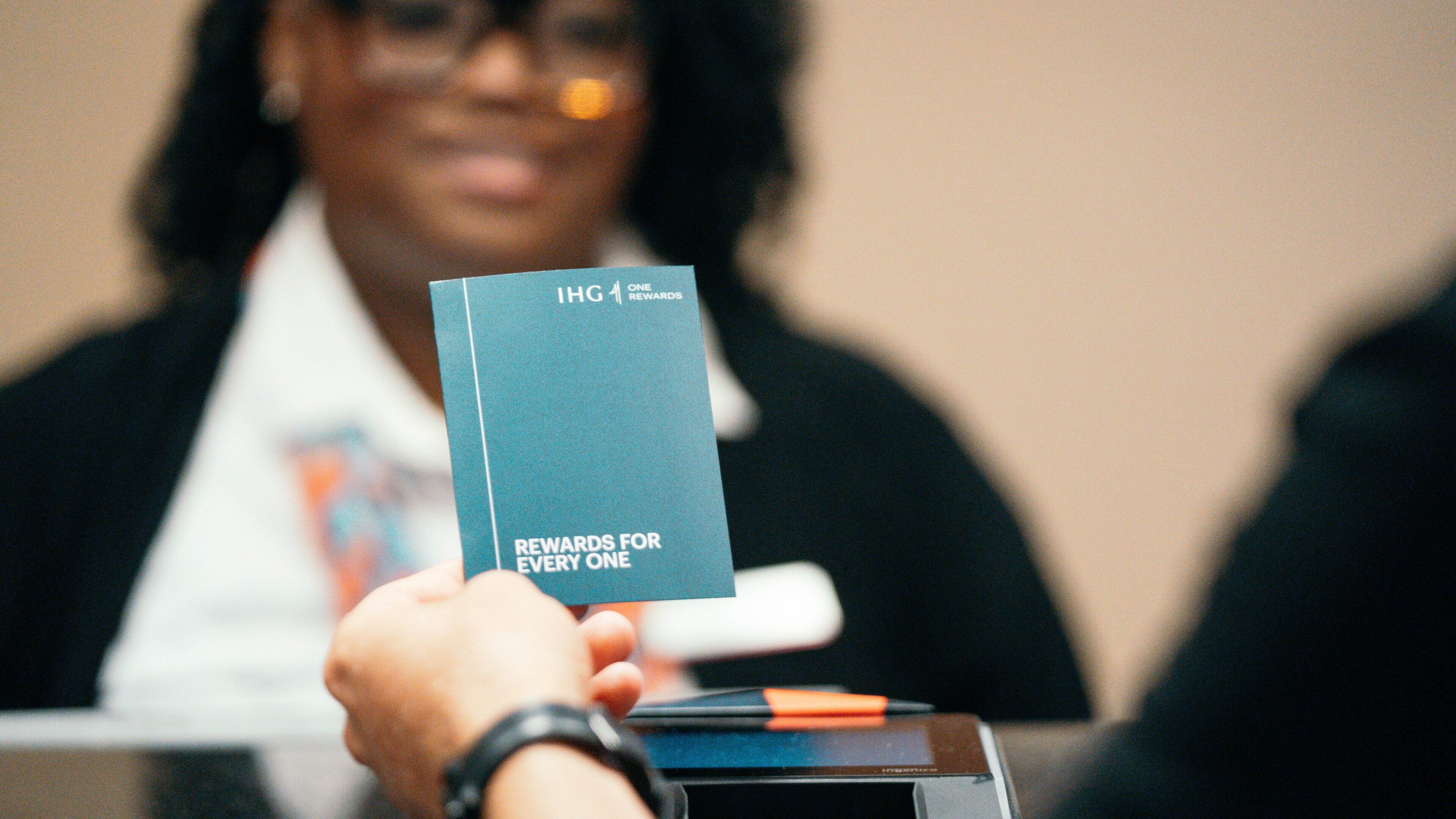 Una persona sosteniendo una tarjeta con el texto "IHG Rewards" y "RECOMPENSAS PARA TODOS".