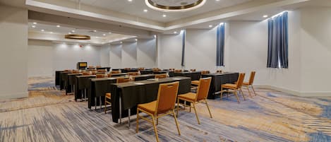 Un salón de conferencias con varias mesas y sillas, una alfombra estampada y un diseño moderno del techo.