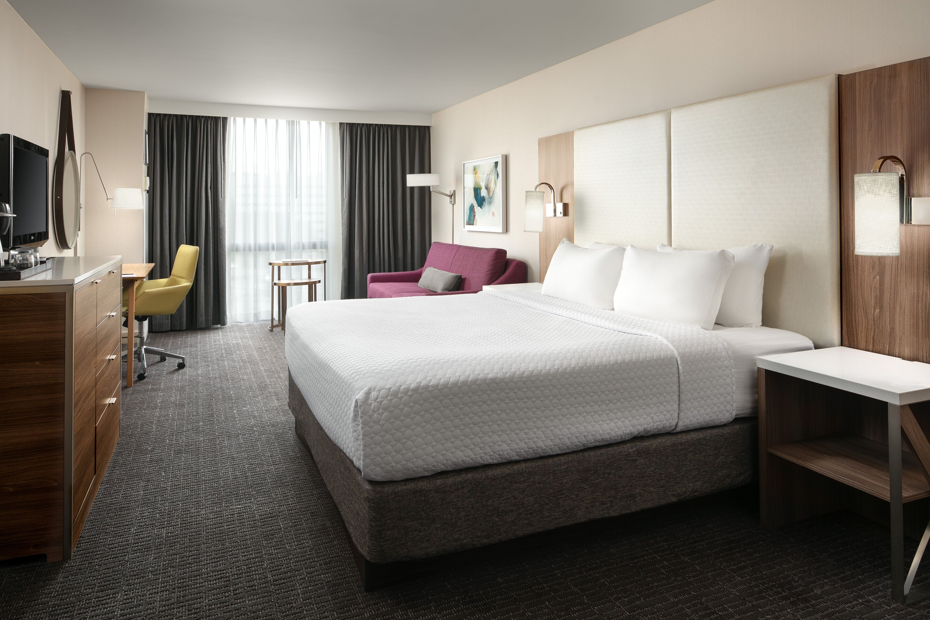 Een hotelkamer met een groot bed, een bureau met stoel, een televisie en een raam met gordijnen.