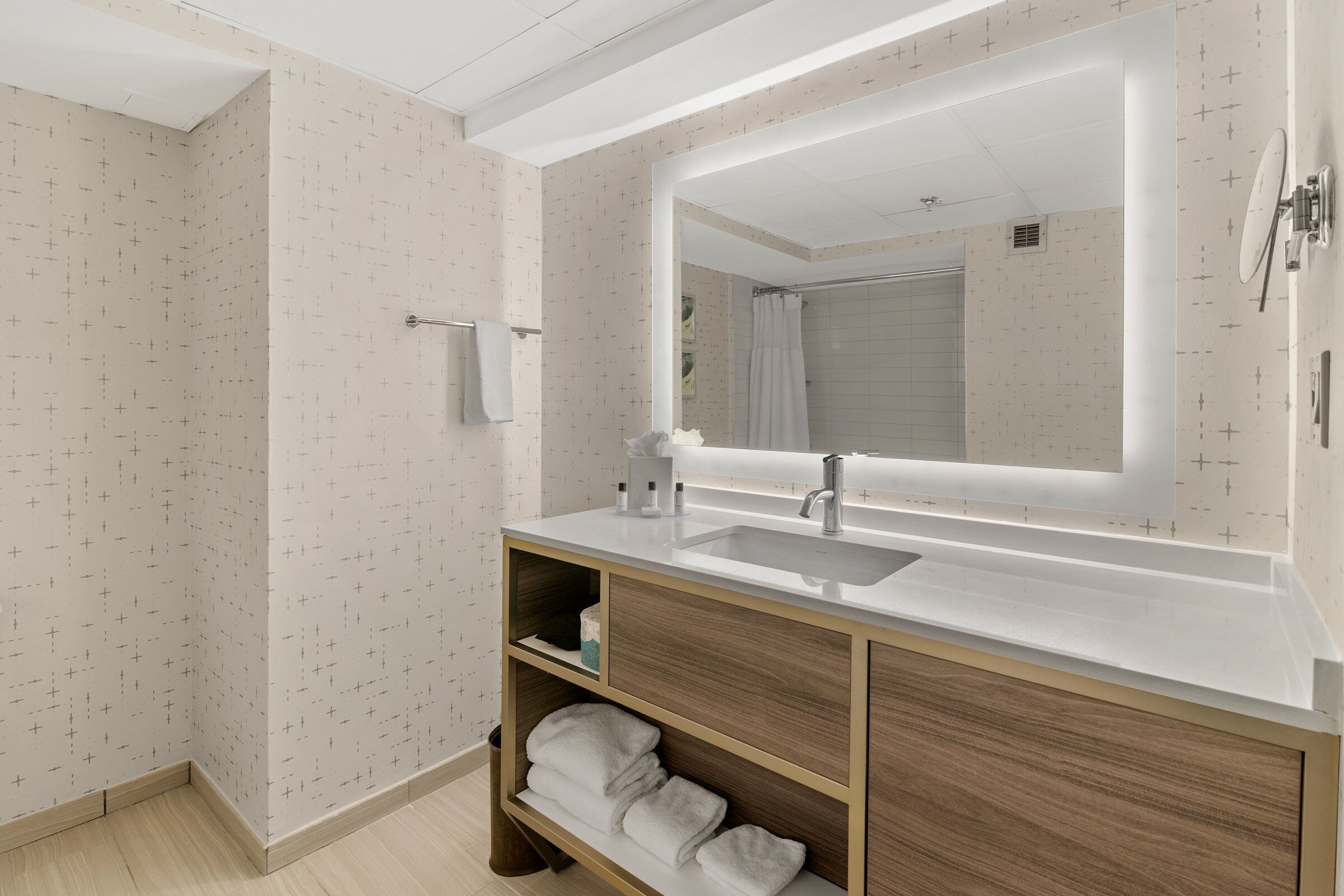 Un baño moderno con un espejo grande, lavamanos blanco y tocador de madera.