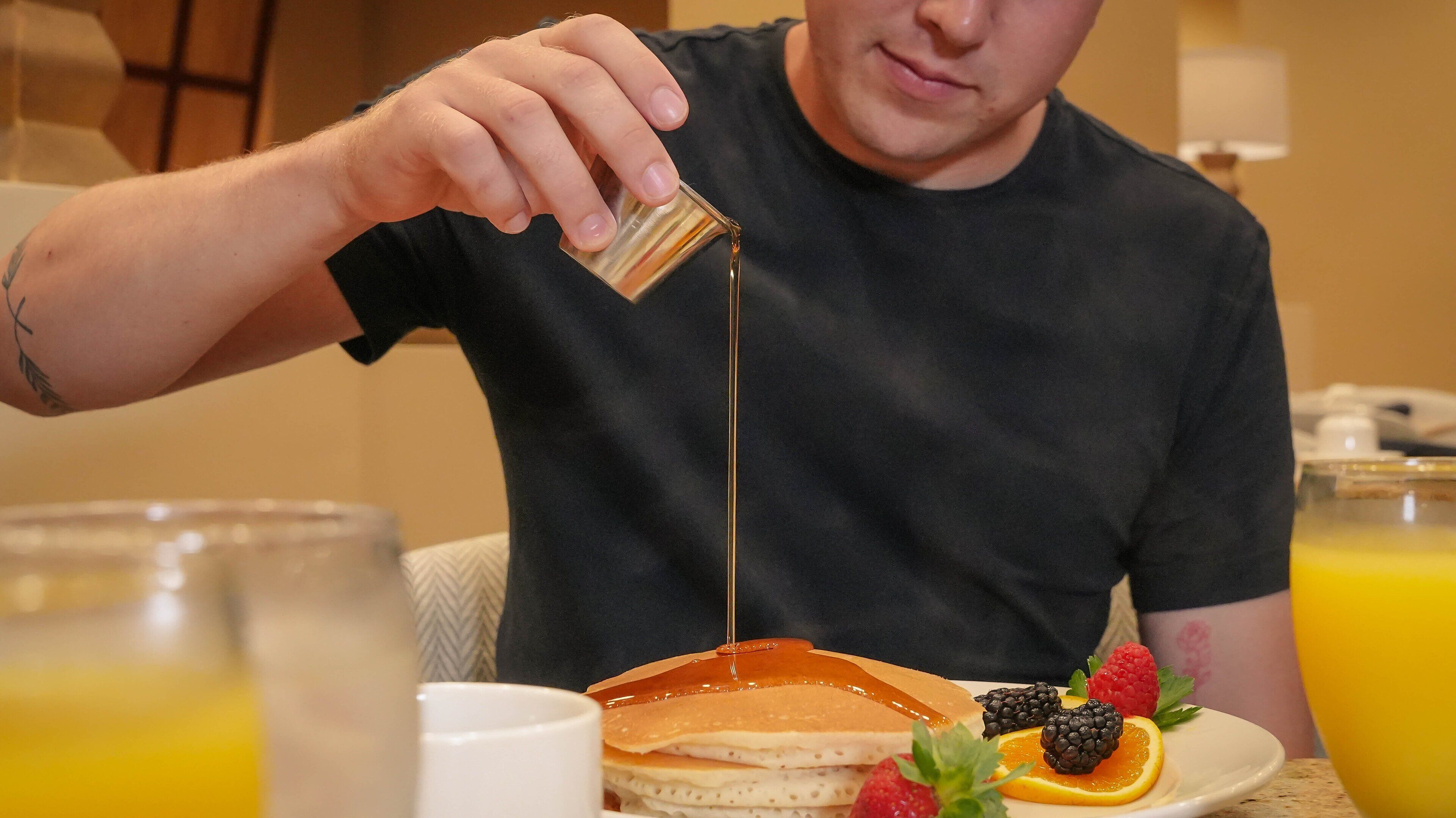 Iemand giet siroop over pannenkoeken met aardbeien en bramen op een bord.