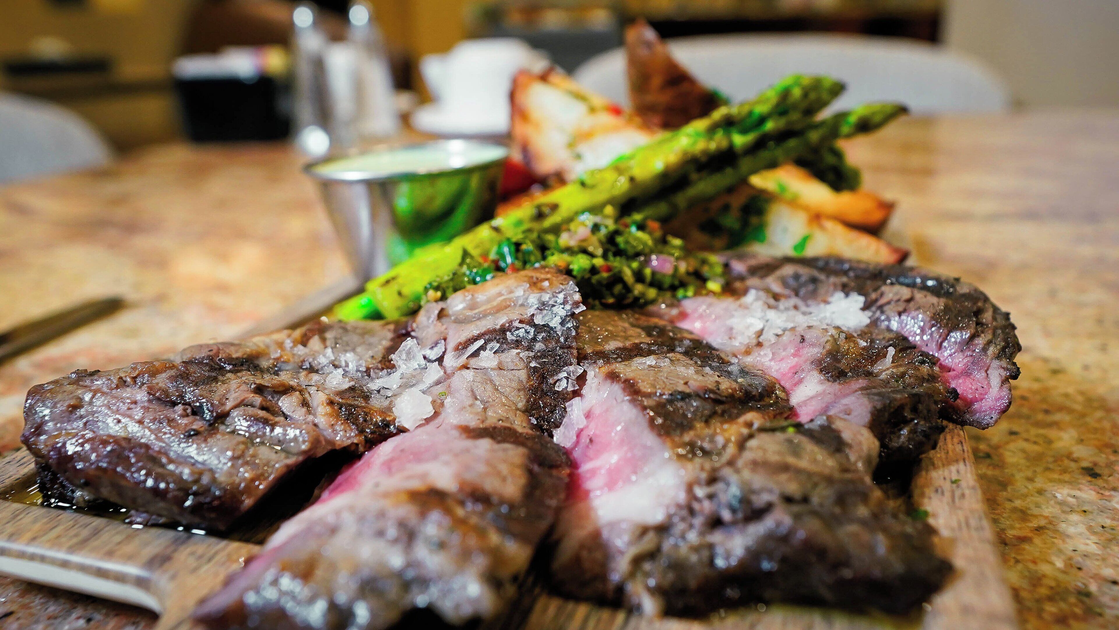 Una tabla de madera con bistec en rodajas, espárragos y papas al horno.