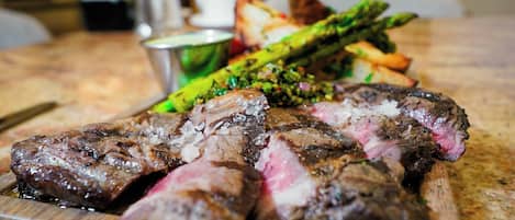 Una tabla de madera con bistec en rodajas, espárragos y papas al horno.