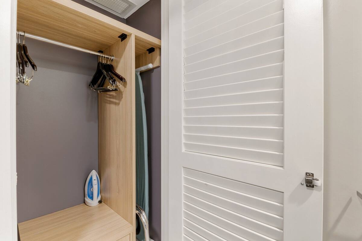 Een inloopkast met een houten plank, hangende kleding en een strijkplank.