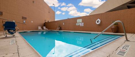 A swimming pool with a lifeguard chair, lounge chairs, and a lifebuoy on the wall.