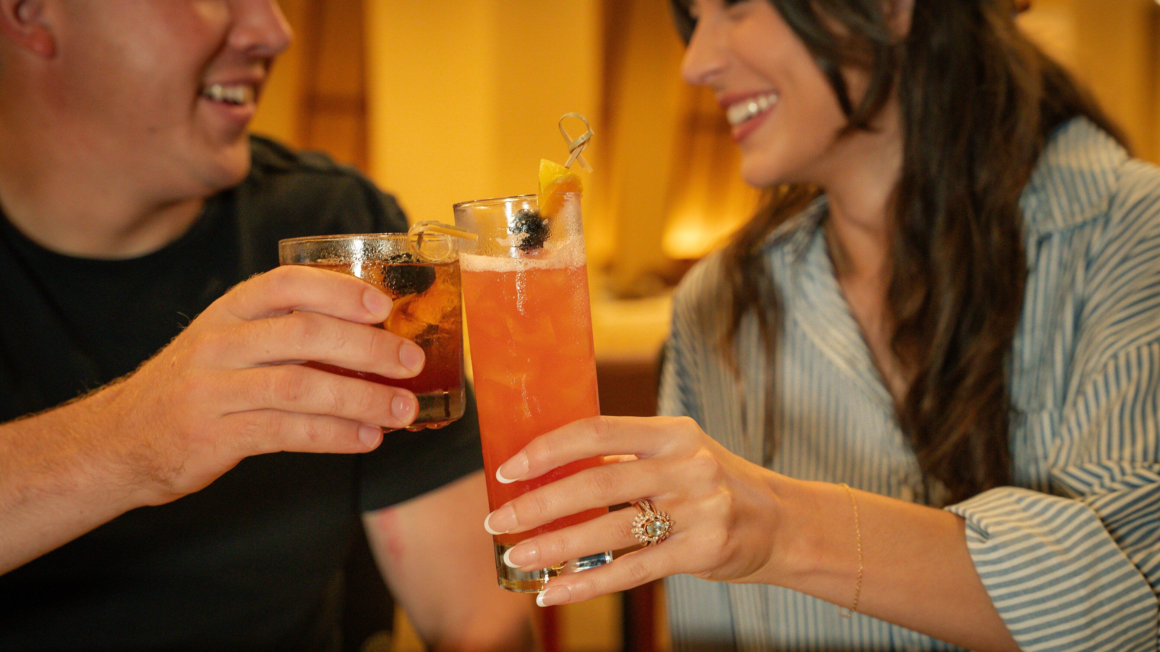 Two people holding glasses of a red beverage with ice and garnishes.