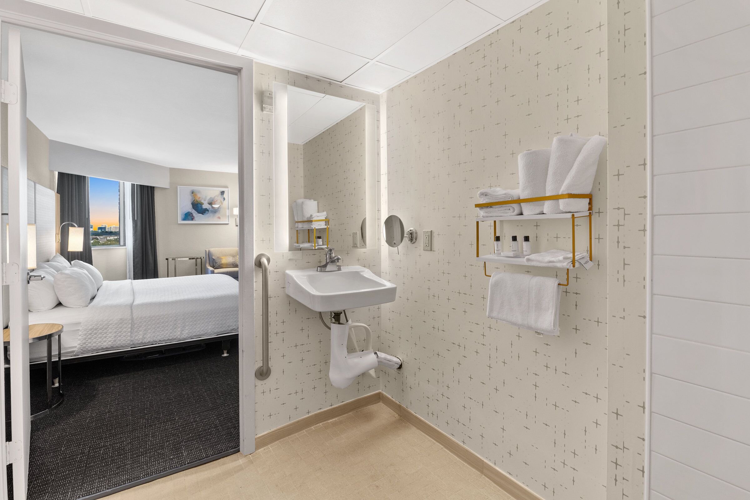 A hotel room with a bed, a bathroom with a sink, and a towel rack.