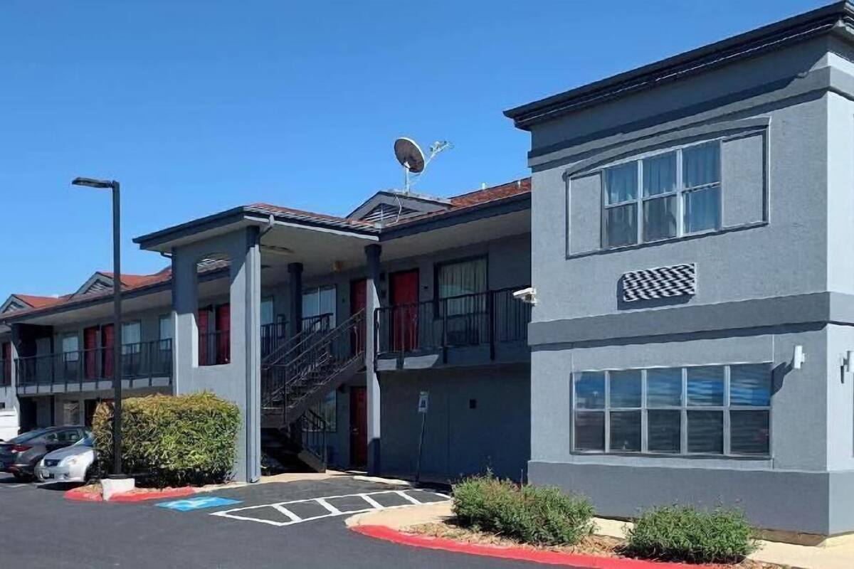 Un edificio a più piani con tetto piatto, un'antenna parabolica e un parcheggio con posti delimitati.