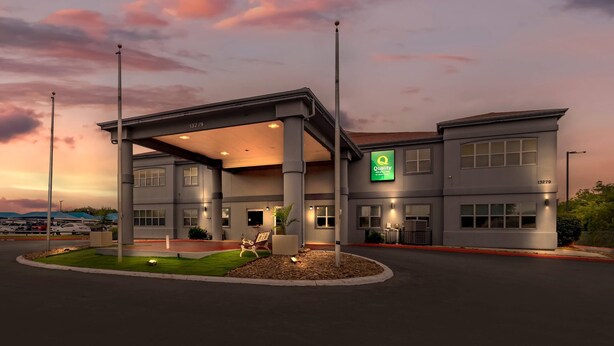 A modern hotel with a covered outdoor area, a green sign, and a parking lot. - Quality Inn & Suites Near Six Flags and Medical Center (San Antonio)