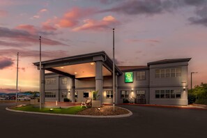 A modern hotel with a covered outdoor area, a green sign, and a parking lot. - Quality Inn & Suites Near Six Flags and Medical Center (San Antonio)