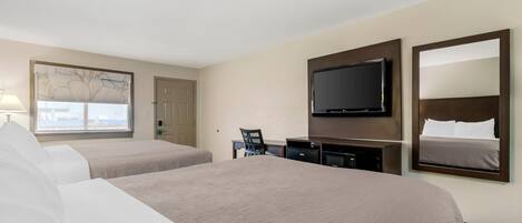 Quarto de hotel com duas camas, uma escrivaninha, televisão e uma janela grande.