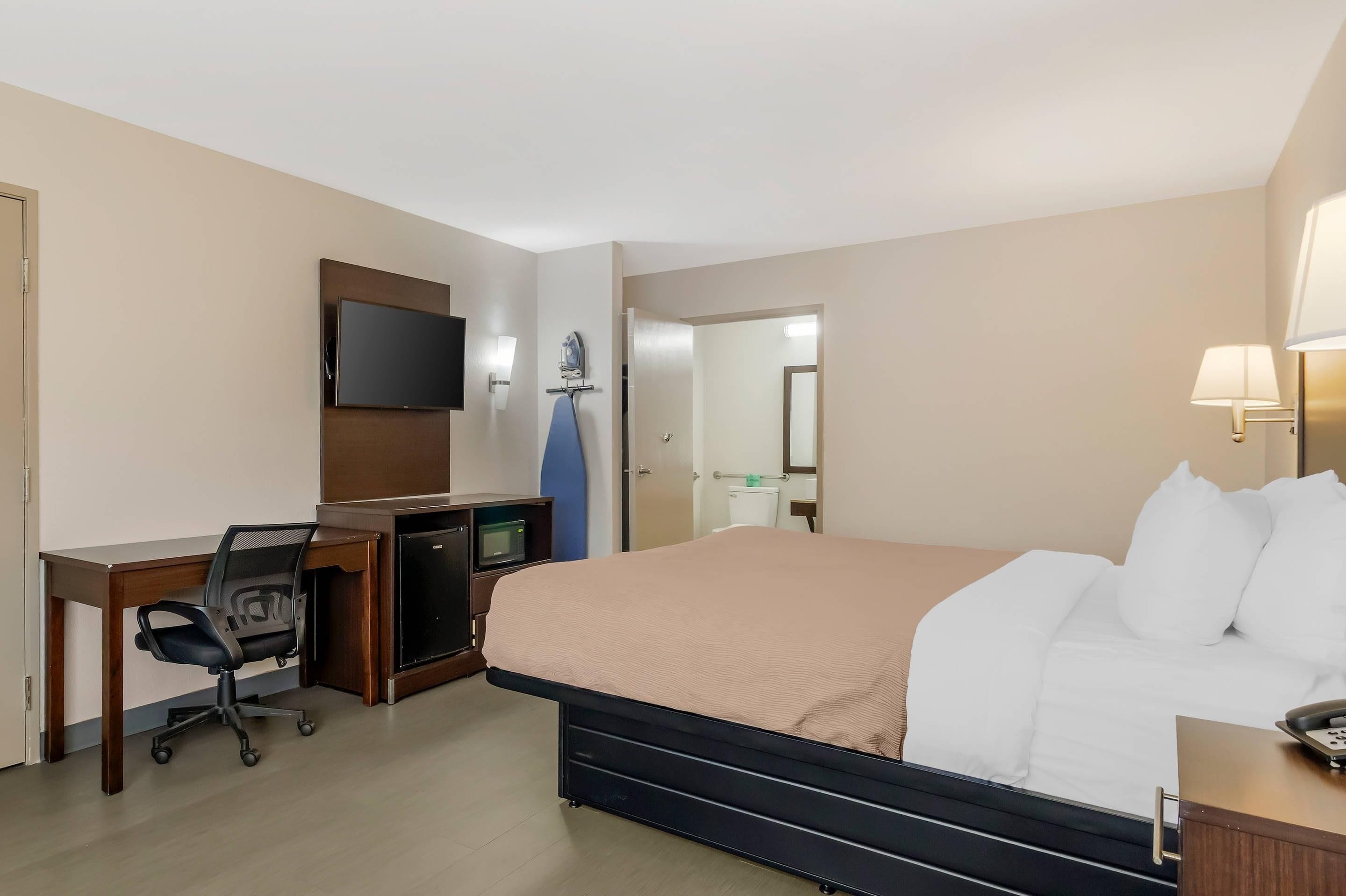Een hotelkamer met een bed, bureau, stoel, televisie en een badkamer die door een open deur zichtbaar is.