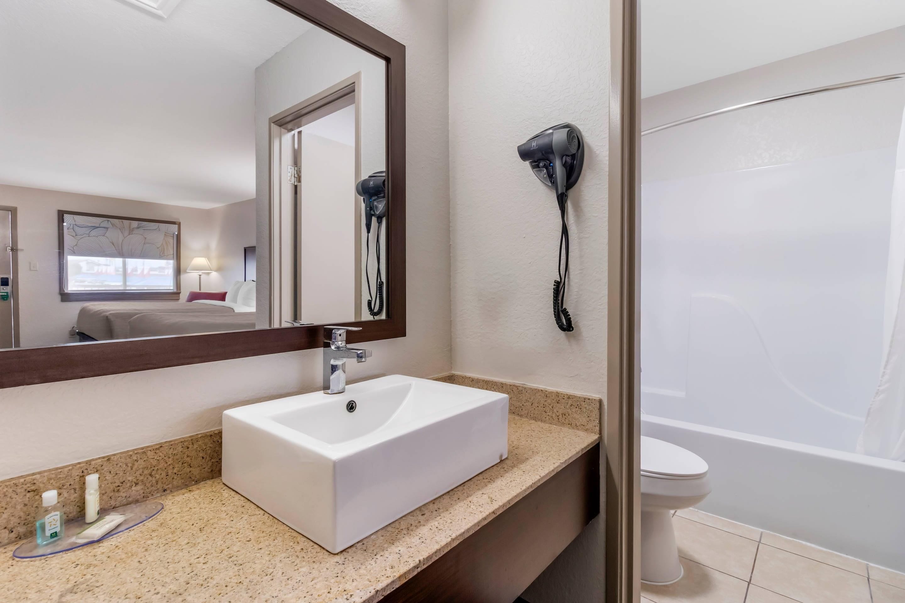 A bathroom with a white sink, a mirror, a hairdryer mounted on the wall, and a bathtub.