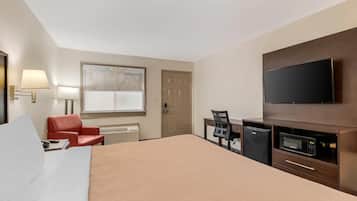 Una habitación de hotel con cama, escritorio, silla, televisor y microondas.