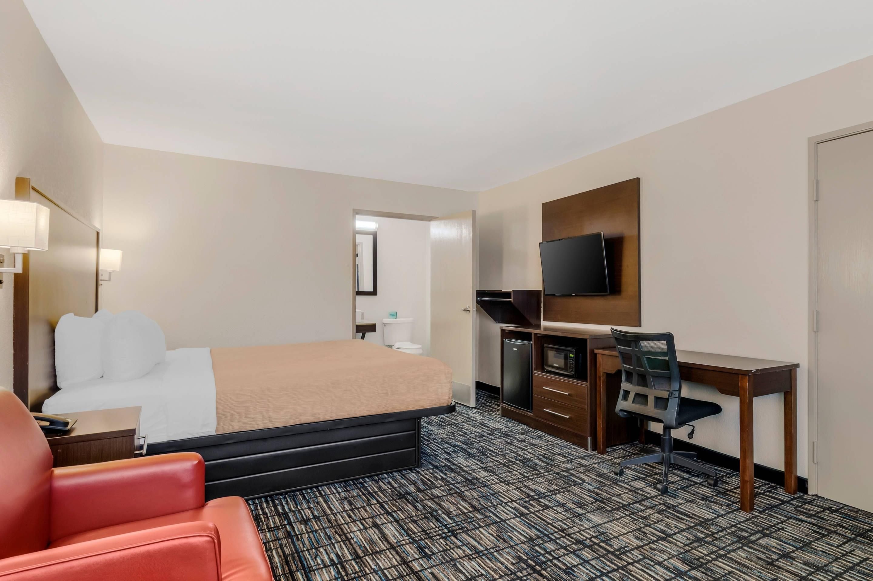 Une chambre d’hôtel équipée d’un lit, d’un bureau, d’une chaise, d’une télévision et d’un petit réfrigérateur.