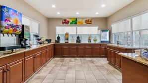 A modern kitchen with brown cabinets, a coffee machine, and a juice dispenser. - Quality Inn & Suites Near Six Flags and Medical Center (San Antonio)
