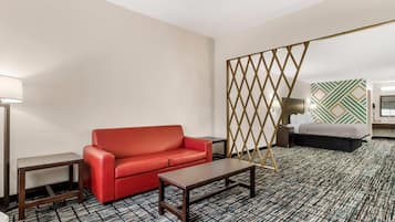 Une chambre d’hôtel avec un canapé rouge, une table basse en bois, une moquette à motifs, un paravent décoratif et un lit agrémenté d’un motif géométrique vert et blanc sur le mur.