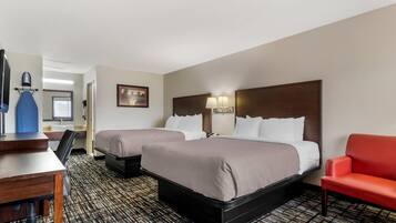 A hotel room with two beds, a desk, a chair, and a television.
