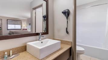 Un baño con un lavamanos blanco, un espejo, un secador de pelo montado en la pared y una bañera.