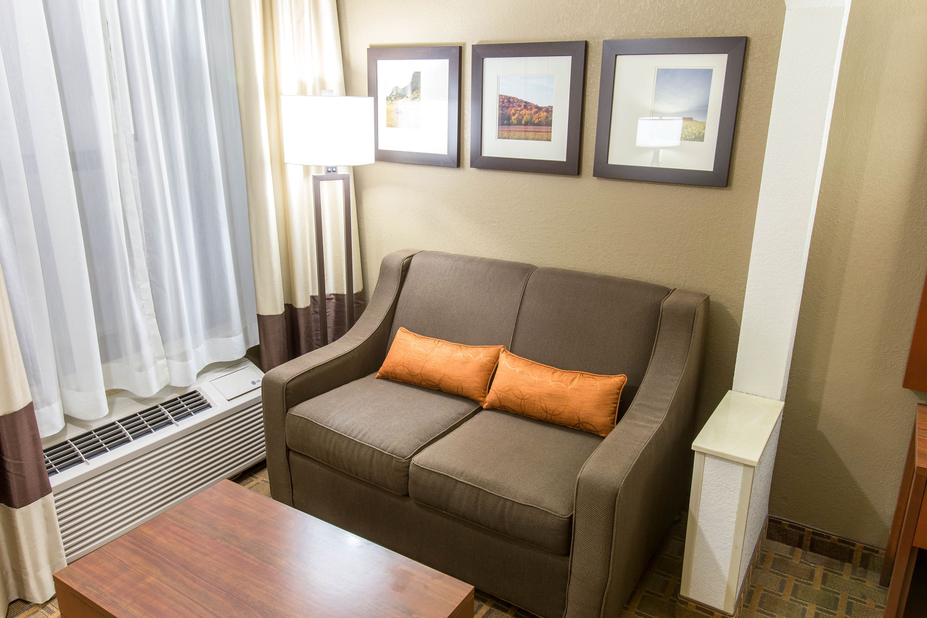 A room with a sofa, a table, and a wall-mounted air conditioner. There are curtains on the window, and three framed pictures on the wall.