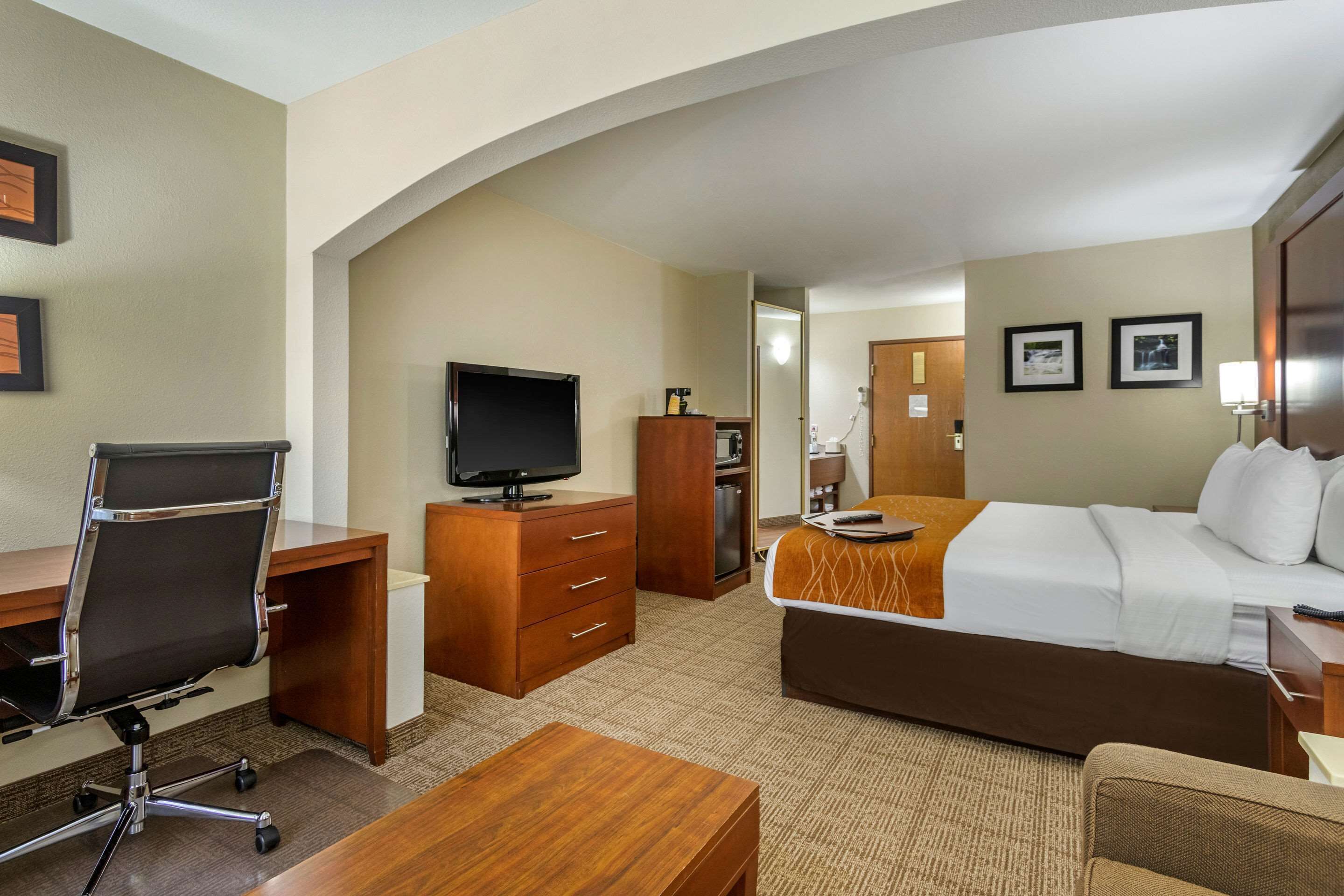 Une chambre d’hôtel comprenant un lit, un bureau avec une chaise, une télévision, une commode et une petite table.