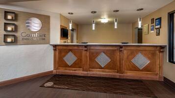 A reception area with a wooden reception desk, a large mirror, and a sign reading "Comfort INN & SUITES."