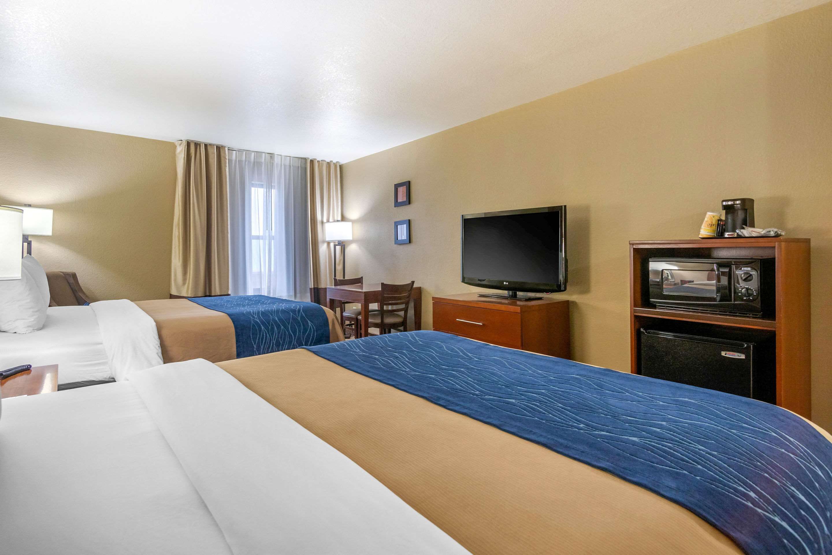 A hotel room with two beds, a desk, a television, a microwave, and a coffee maker.