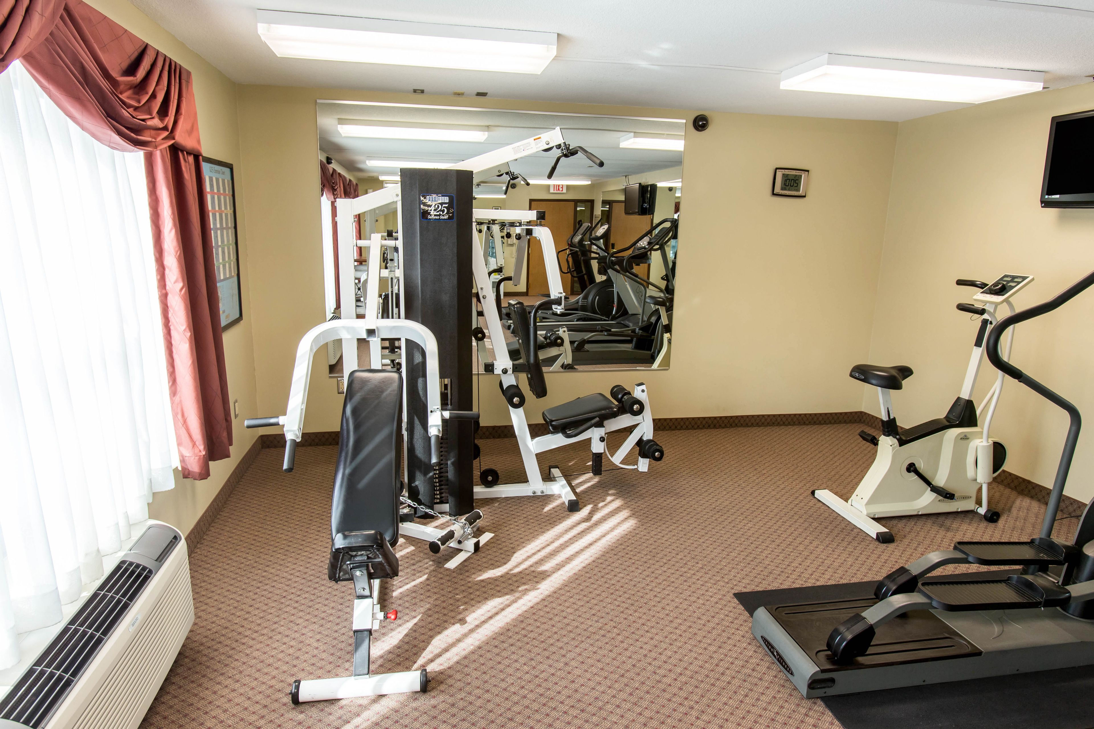 A gym with various exercise equipment, including treadmills and weight machines, and a large mirror on the wall.