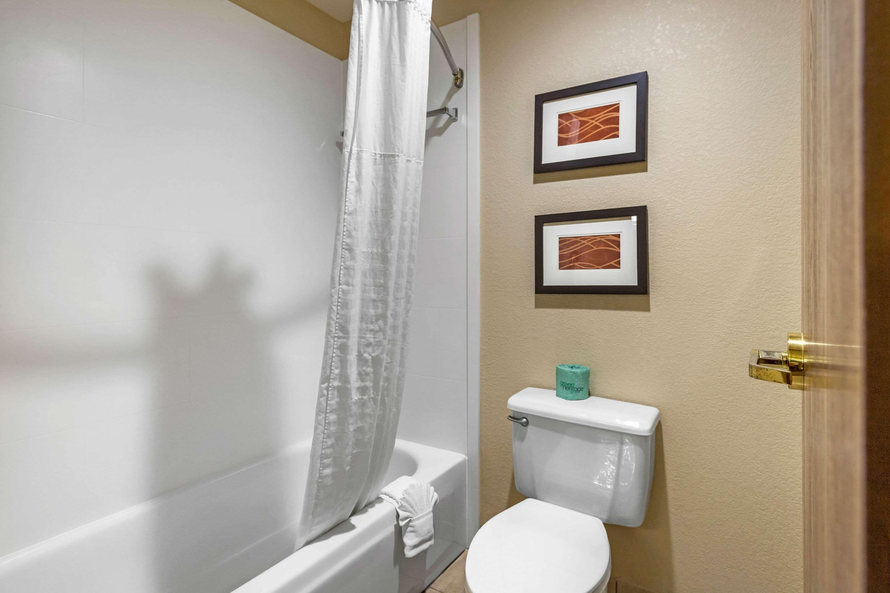 A bathroom with a bathtub, toilet, and two framed pictures on the wall.