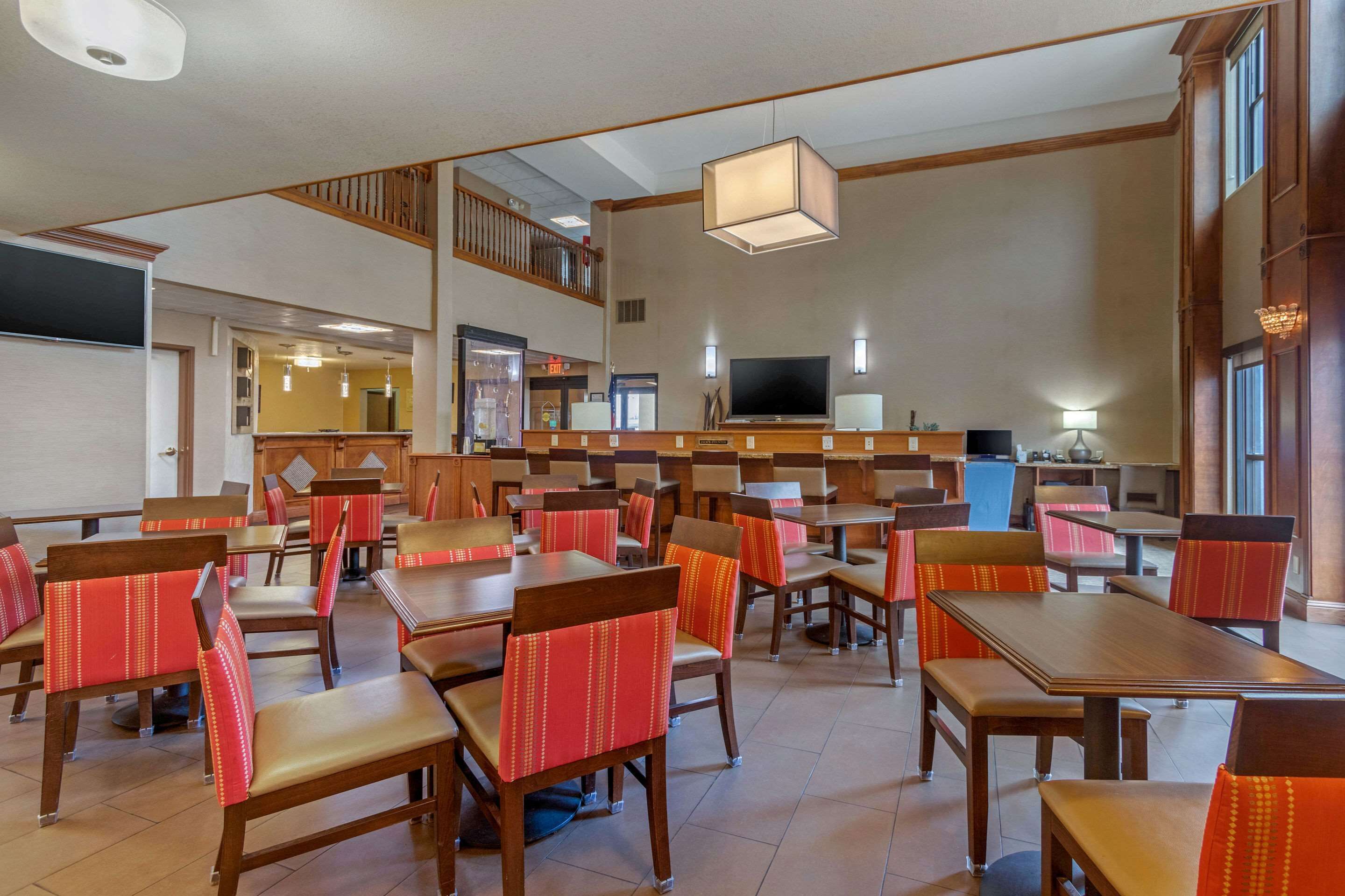 Een restaurantruimte in een hotel met meerdere tafels en stoelen, een televisie en een trap naar een hoger gelegen verdieping.