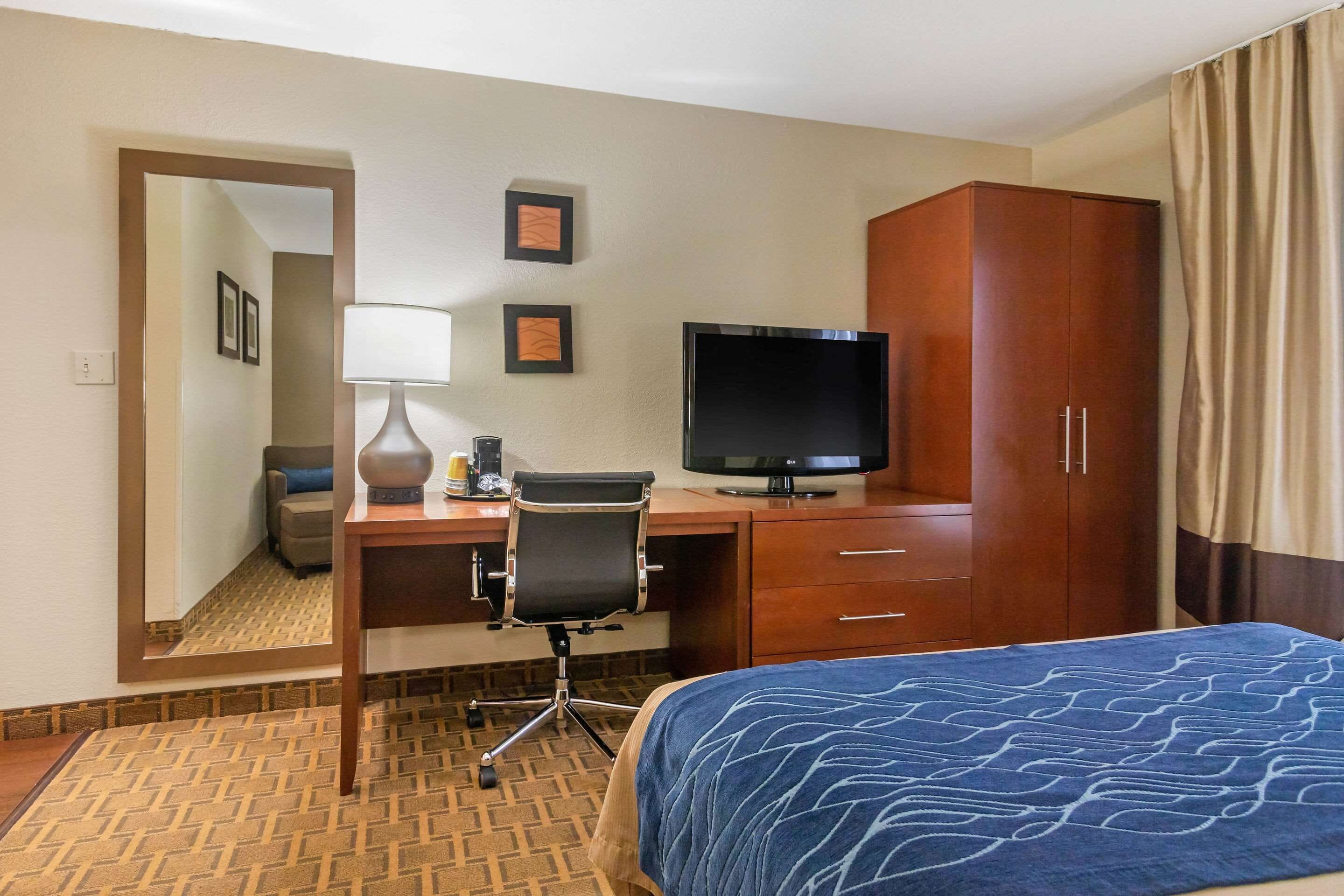 A hotel room with a bed, a desk with a computer, a TV, a wardrobe, and a mirror.