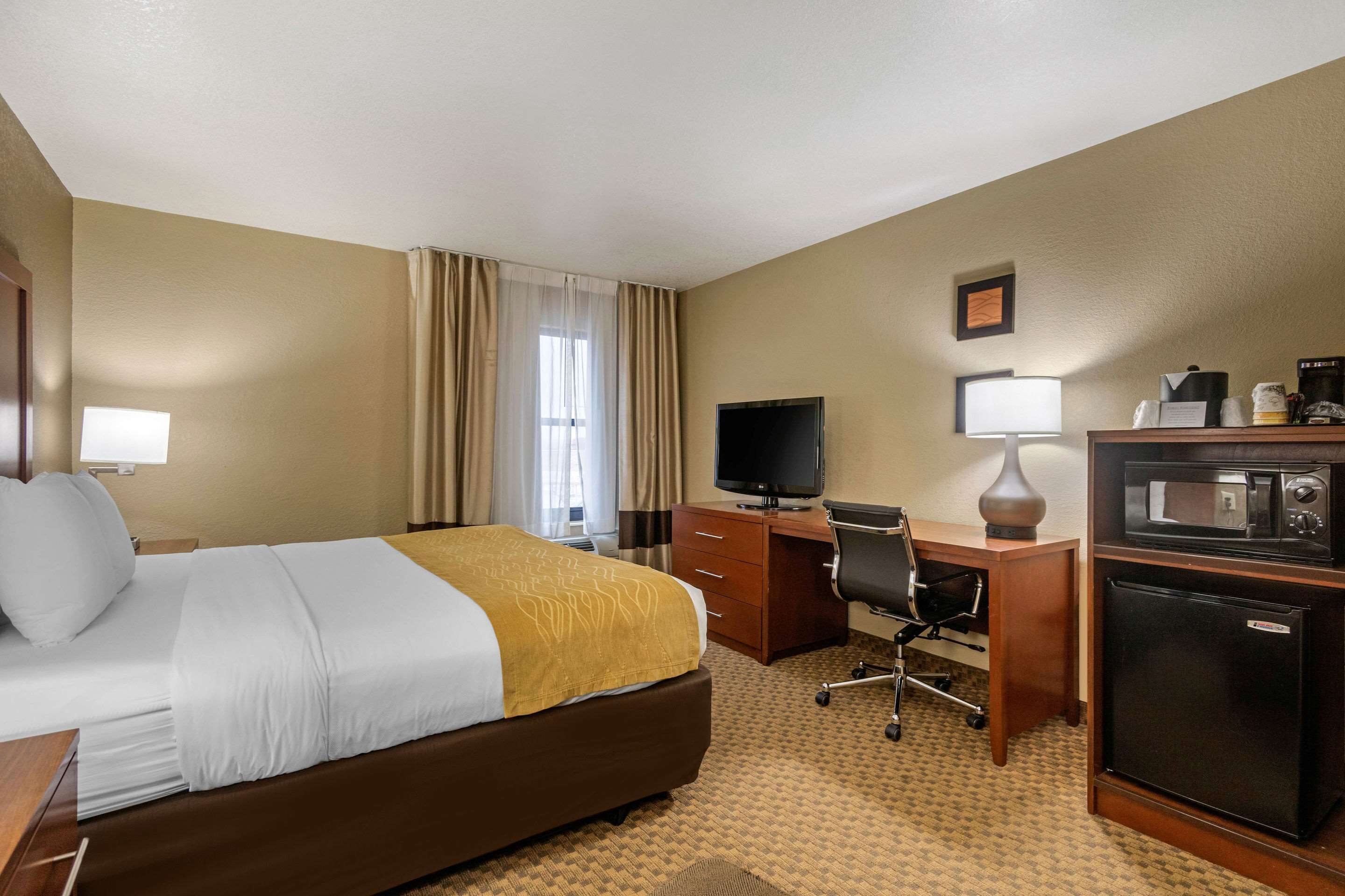 Une chambre d’hôtel équipée d’un lit, d’un bureau, d’une télévision et d’un réfrigérateur.