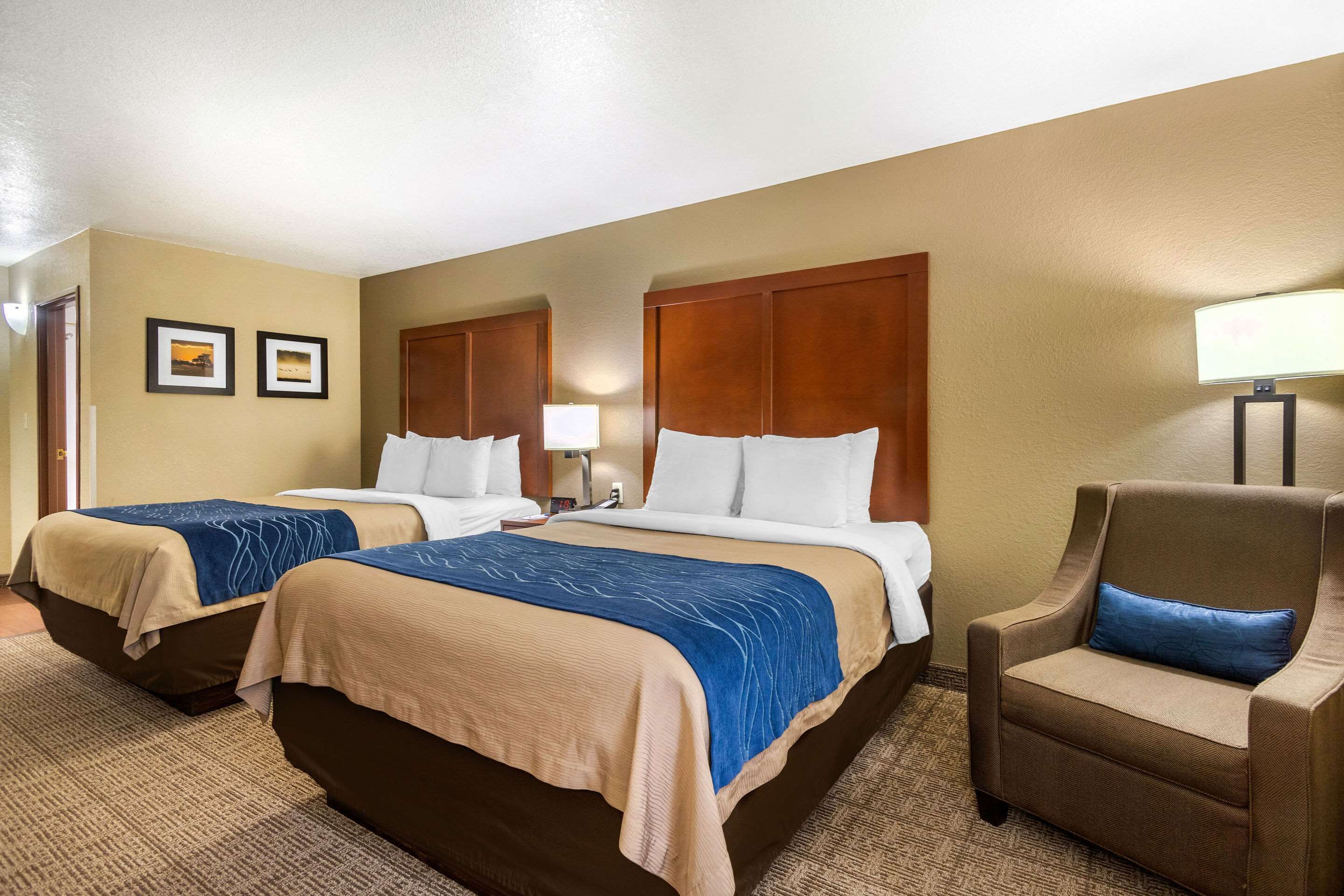 A hotel room with two beds, a chair, and a lamp.