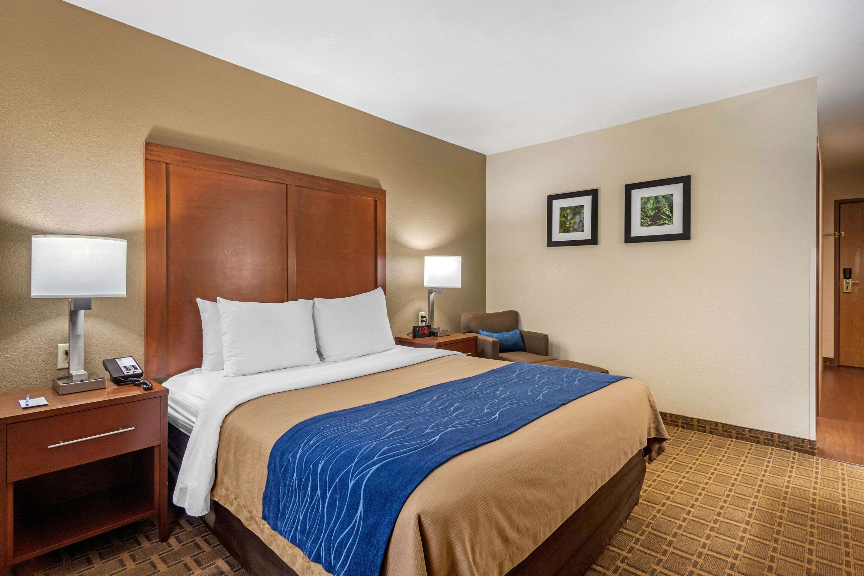 A hotel room with a large bed, two bedside tables with lamps, a chair, and two framed pictures on the wall.