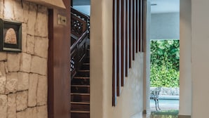 Un interior moderno con una pared de piedra, una escalera de madera y vistas al exterior con vegetación.