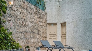 Una piscina con dos sillas reclinables, un muro de piedra y una puerta.