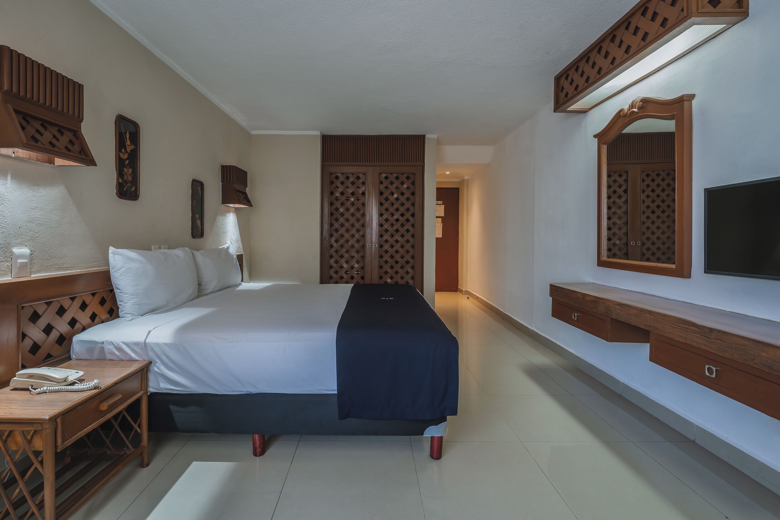A hotel room with a bed, bedside table, lamp, wardrobe, TV, and a mirror.