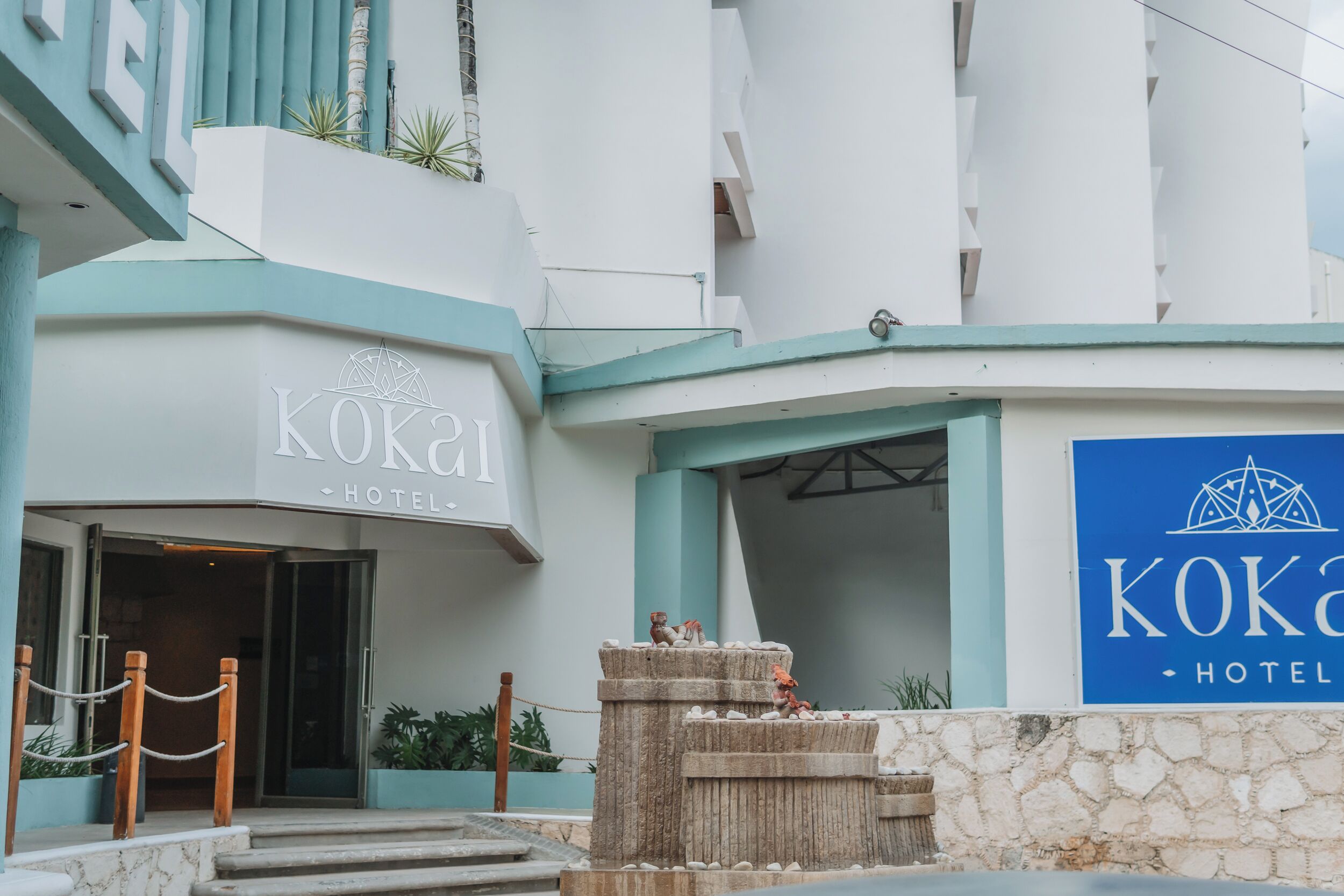 L’extérieur de l’HÔTEL KOKAI se distingue par son entrée imposante, une fontaine en pierre et un panneau bleu.