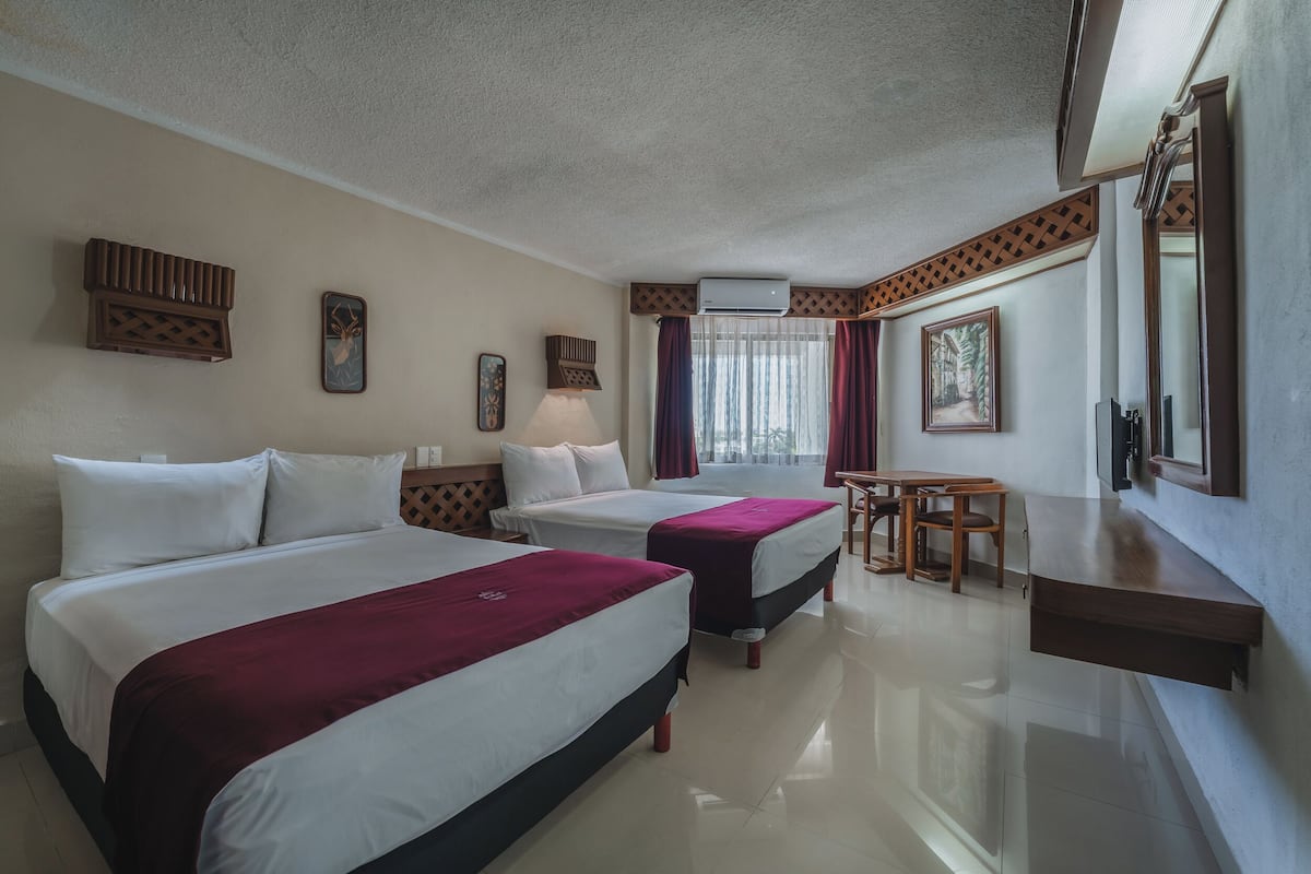 A hotel room with two beds, a desk, a chair, a mirror, and a window with curtains.
