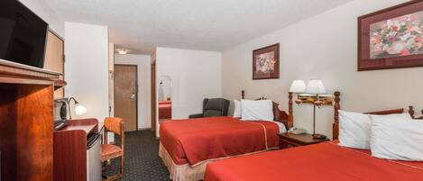 A hotel room with two beds, a desk with a lamp, a chair, a TV, and a painting on the wall.