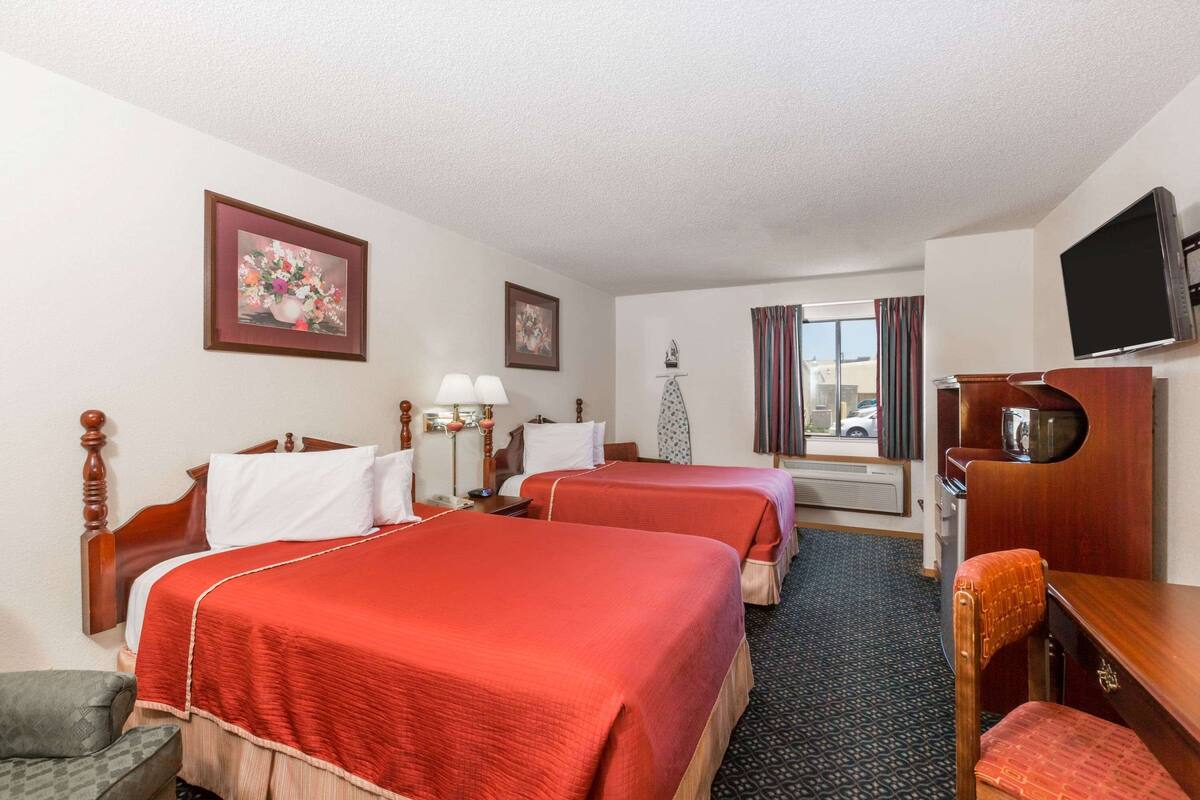 A hotel room with two beds, a television, a desk, and a chair.