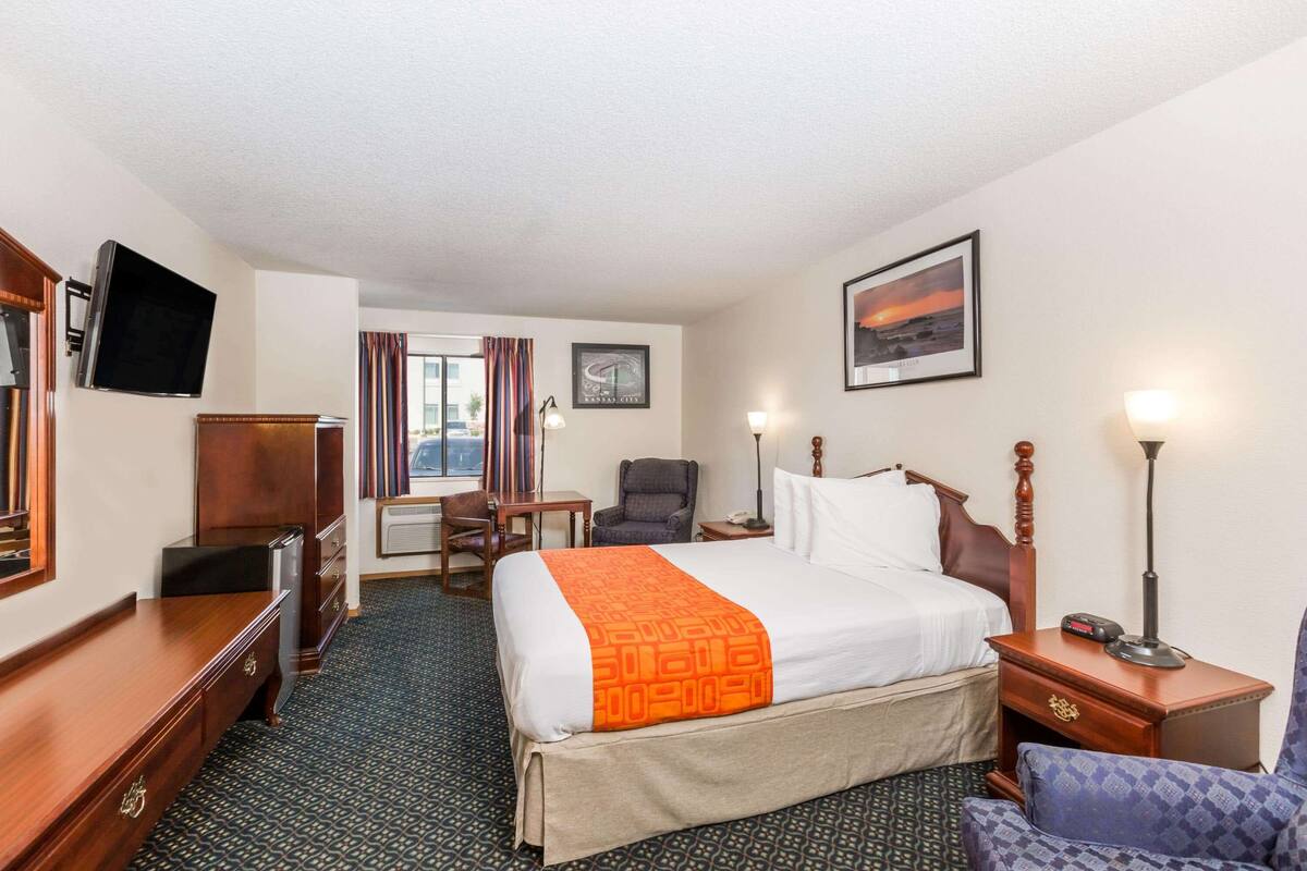 A hotel room with a bed, a desk, a chair, a TV, and a window with curtains.