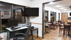 A hotel room with a desk, computer, chair, and a TV. There are multiple tables and chairs in the dining area. - Howard Johnson by Wyndham Wichita Airport (Wichita)