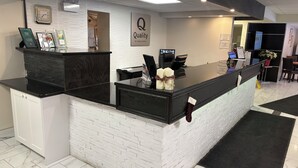 Un mostrador de recepción de hotel con una superficie negra, pared de ladrillo blanco y un letrero que dice 'Quality by Choice Hotels'.