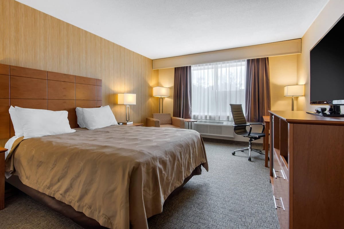 A hotel room with a large bed, a desk with a chair, a TV, and a window with curtains.