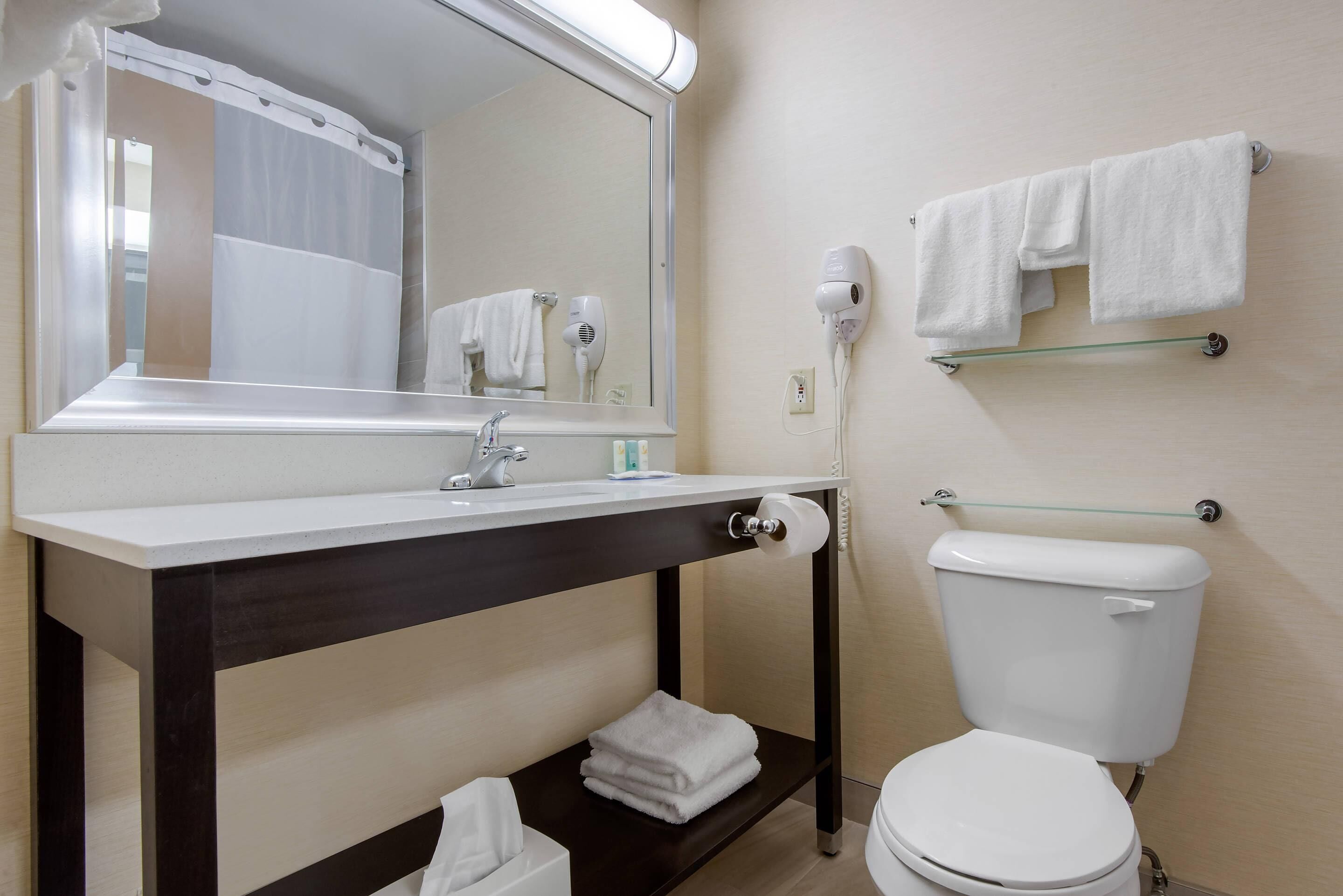 Een badkamer met een witte wastafel, donkerdressoir, spiegel, handdoekhouder en toilet.