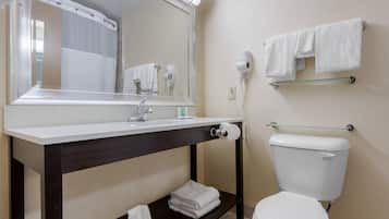 Et badeværelse med hvid vask, mørkt kommodebord, spejl, håndklædestang og toilet.