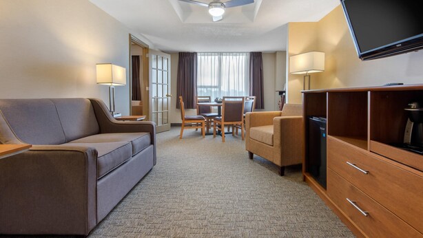 Una habitación de hotel con sofá, una mesa de comedor con sillas, televisor y ventilador de techo.