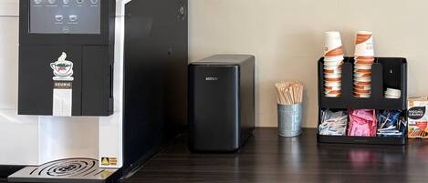 A coffee machine with a digital interface, a trash bin, and a coffee cup holder with disposable cups.